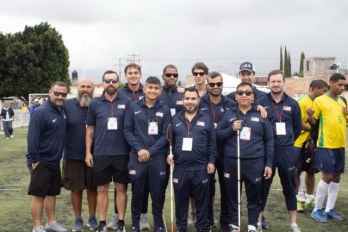 Twelve people posing for a group photo outdoors on a football pitch